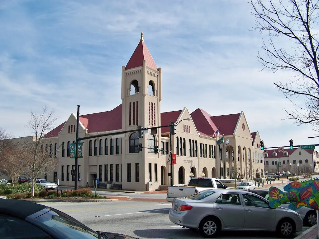 Anderson City Hall, a tan building with a bell tower and red roofs, on a downtown corner with traffic lights and parked cars